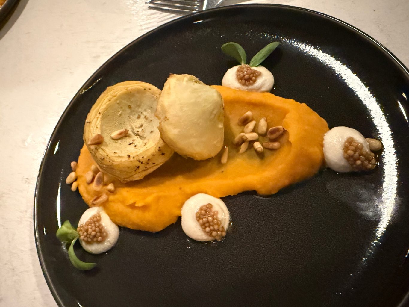 Artischokenherzen auf Kürbispüree mit Cashewcreme Gericht mit Kürbispüree, panierten Kugeln und Nüssen, dekoriert mit Kräutern und Sahne.